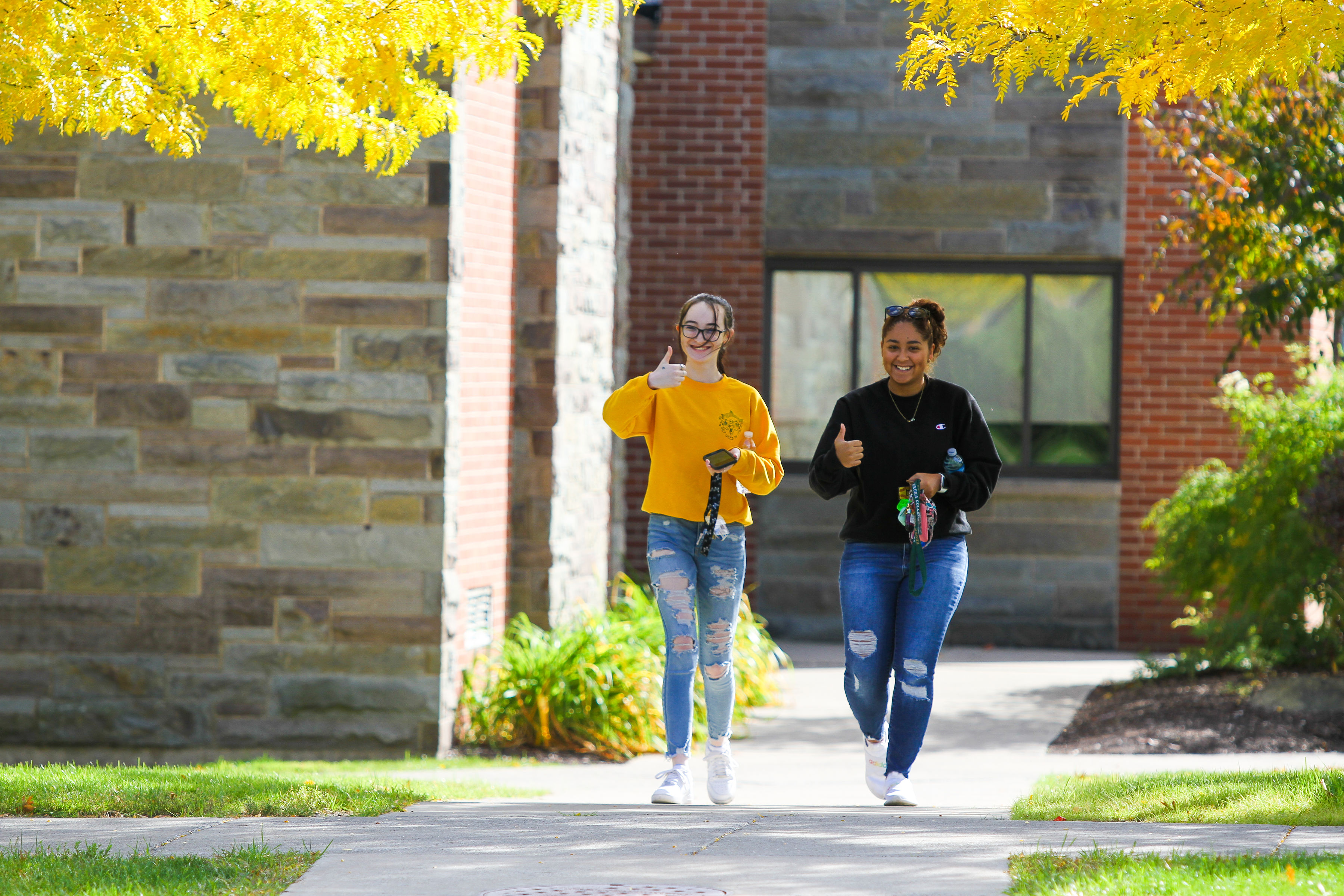 Two students walking out of Saunders Hall, one giving a thumbs up