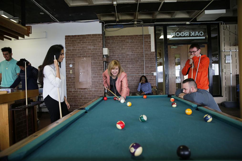 Amy Storey playing a game of pool with students standing around the table watching her take a shot