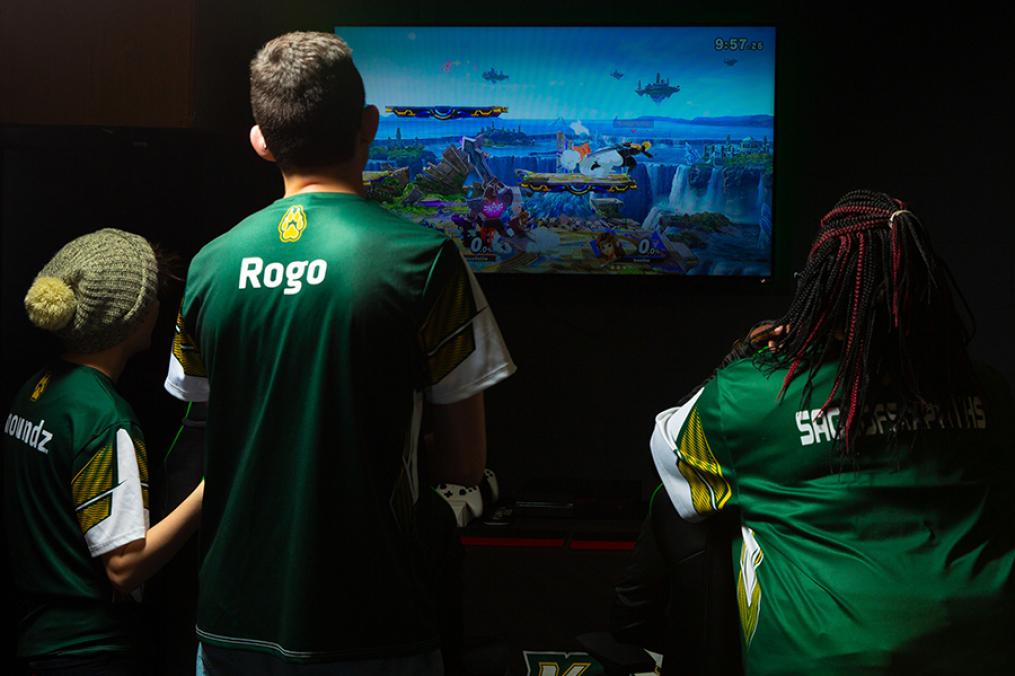 Three students gather around an esports screen