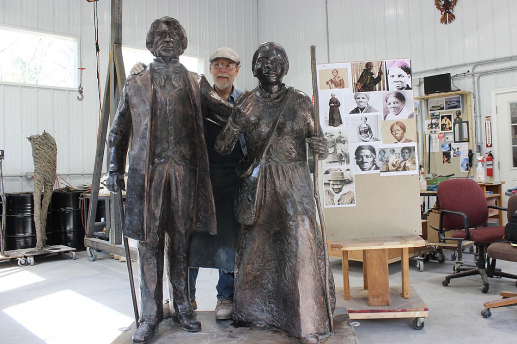 In creating his works, Professor Emeritus Dexter Benedict uses a photo board to help bring expression to those he sculpts, like the one he used for Harriet Tubman (r). Dexter poses in the middle of his latest work.