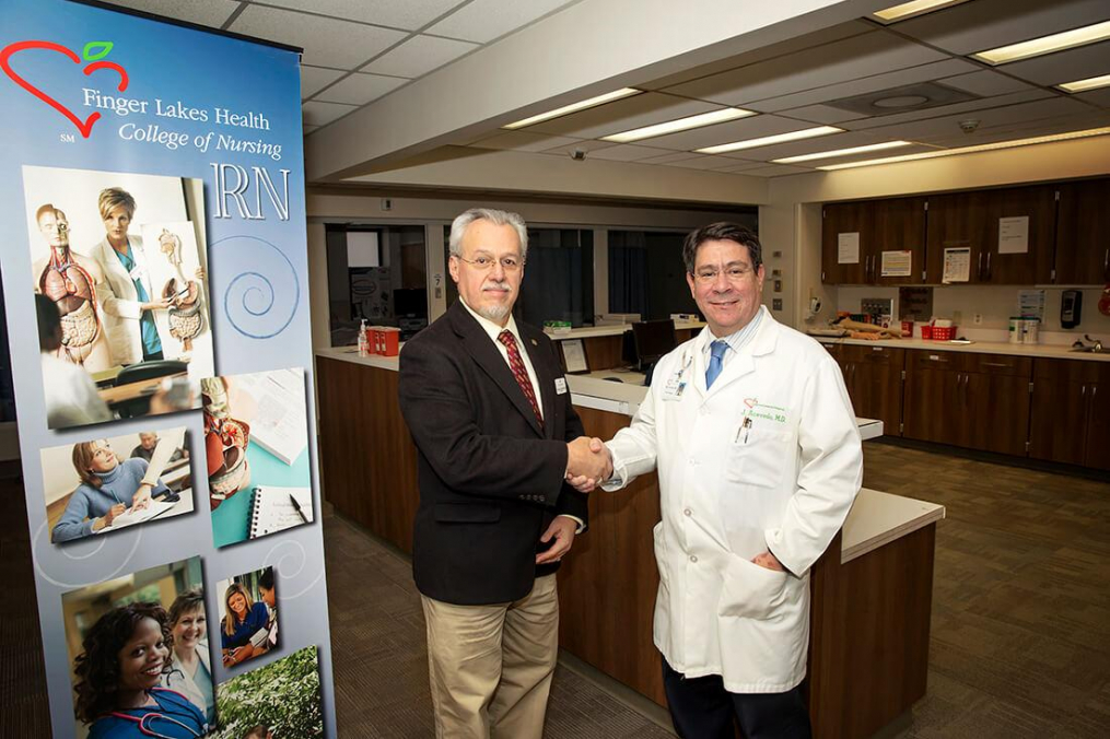 Keuka College President Jorge L. Díaz-Herrera, Ph.D., and Finger Lakes Health President & CEO Jose Acevedo, M.D., M.B.A. shake hands in the Finger Lakes Health College of Nursing laboratory. 