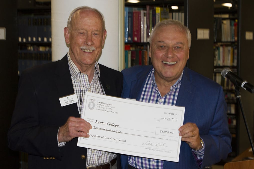 two men holding a check for $5,000 in the library. The check is made out to Keuka College. 