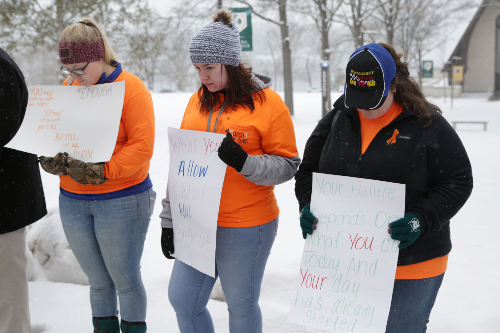 Three Keuka College students hold posters they made in a show of solidarity with the national #ENOUGH movement during an event that included 17 minutes of silence on Wednesday, March 14.