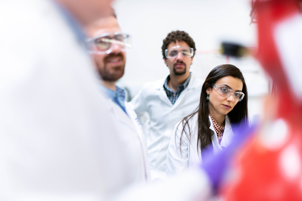 men and women in a lab wearing lab coats and protective eye glasses