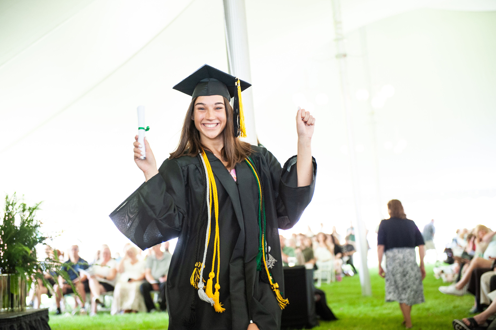 A graduate walking off the stage smiling having just received her diploma 