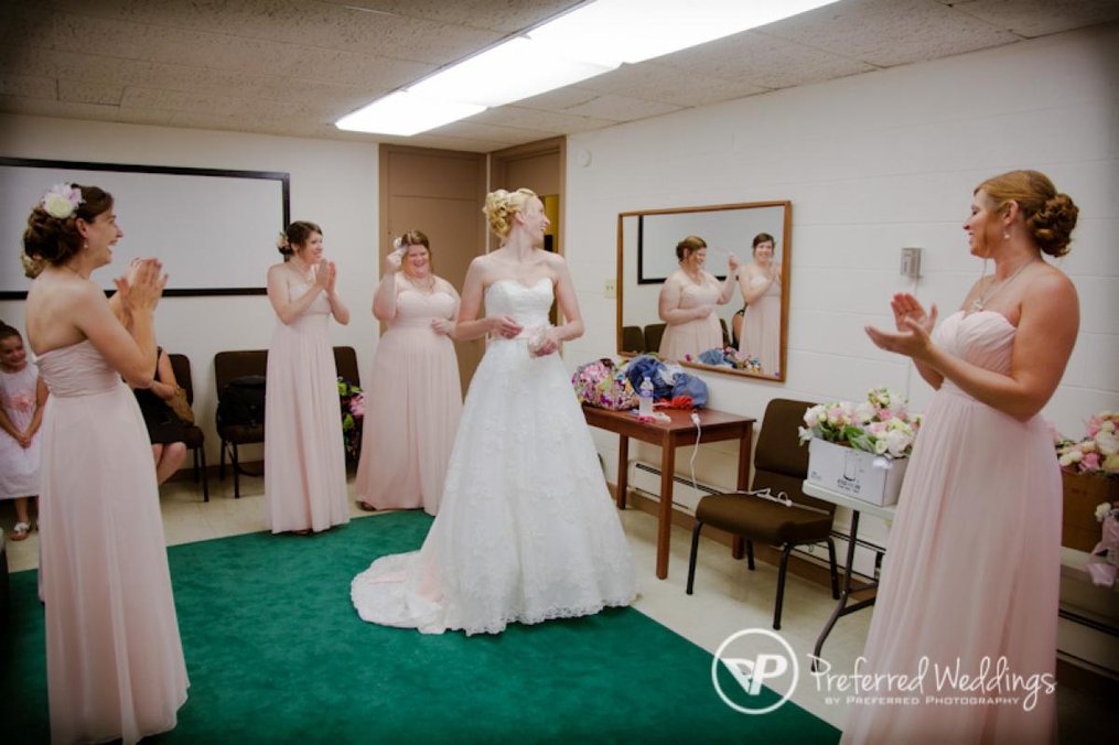 Bridesmaids standing around a bride in her dress before a ceremony