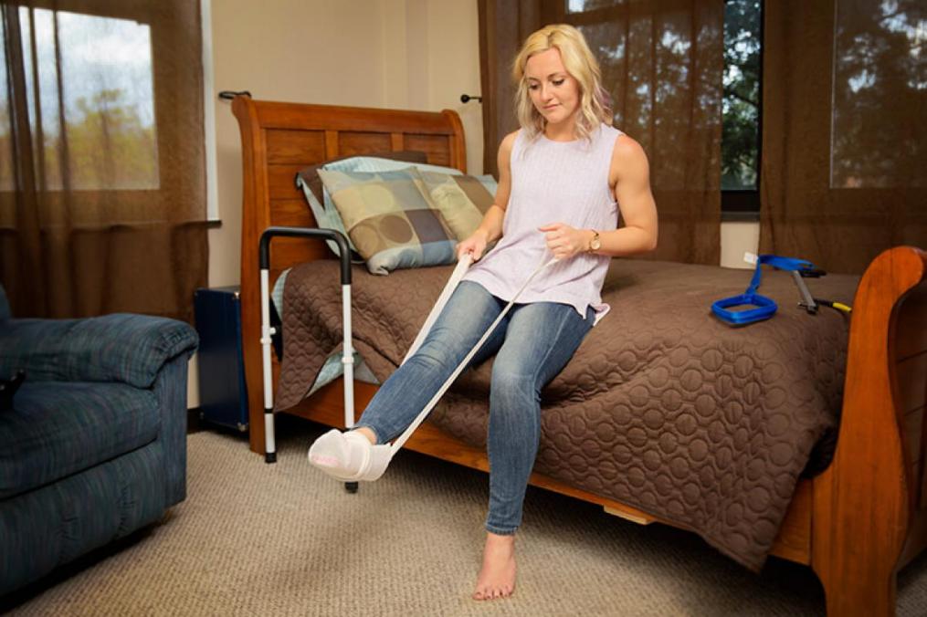 Young woman sitting on a bed with her foot in a sling