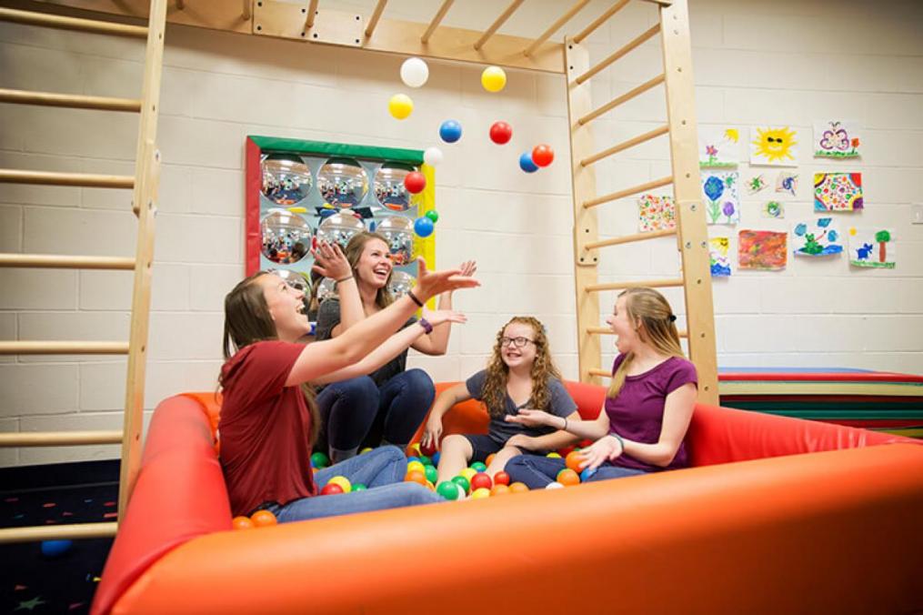 students with children in a play room throwing plastic balls in the air