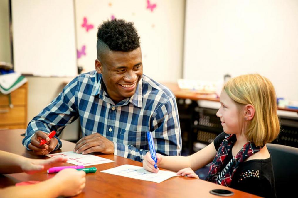 Student with a child sitting at a table drawing a picture with them