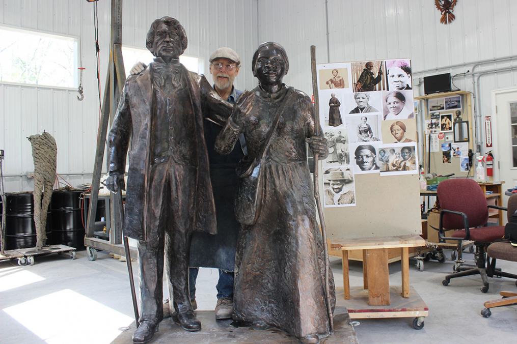 In creating his works, Professor Emeritus Dexter Benedict uses a photo board to help bring expression to those he sculpts, like the one he used for Harriet Tubman (r). Dexter poses in the middle of his latest work.