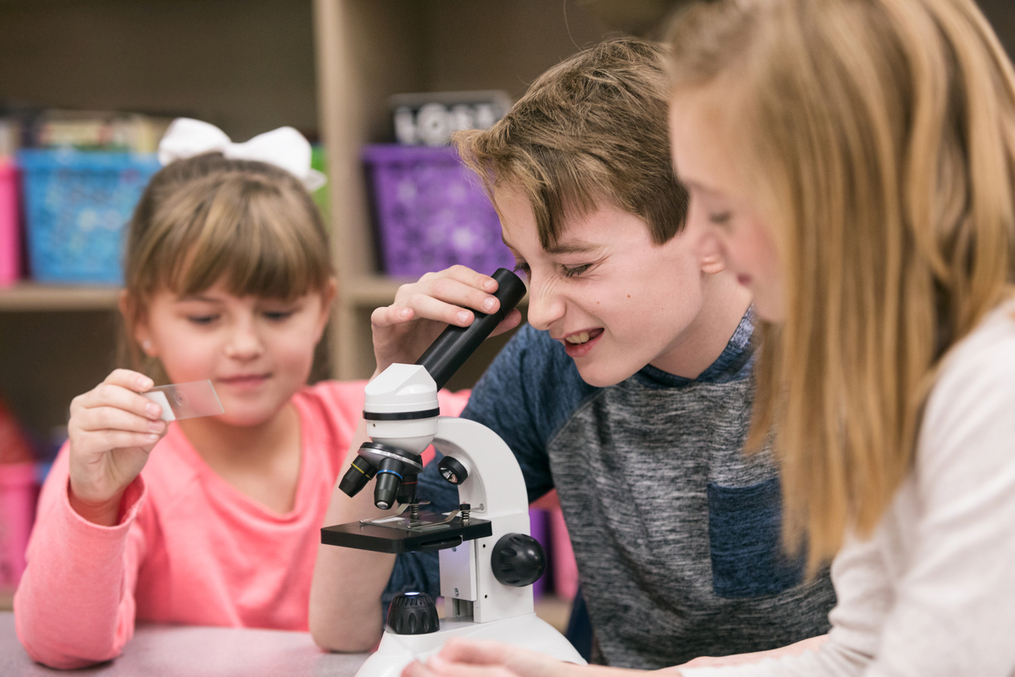 Teacher working with students looking into a microscope 