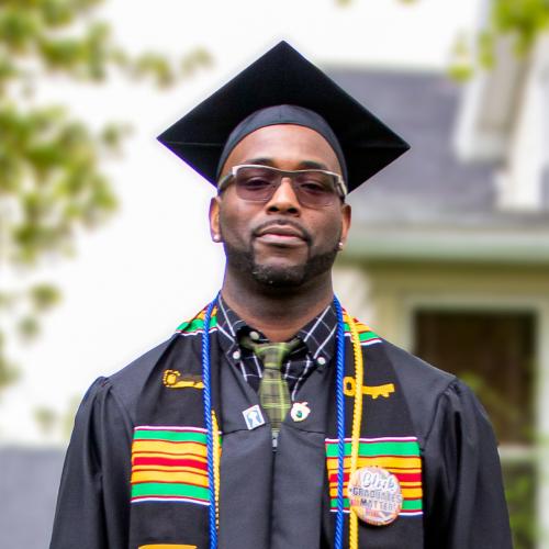 Caswell Smith is a Keuka College MSW graduate. Here, he stands outside his home wearing his cap, gown, and stole.